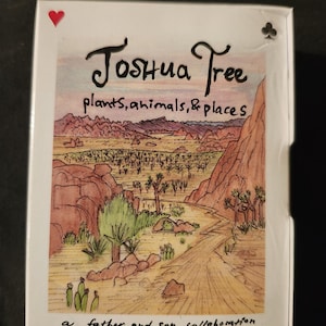 May include: A deck of playing cards featuring a desert landscape illustration with the words "Joshua Tree plants, animals, & places." The deck is a father and son collaboration with 52 sketches by Serge and Aaron Trotter. The card corners show the suit symbols.