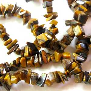 K&ouml;nnte beinhalten: Eine Str&auml;hne aus Tigerauge-Edelsteinkugeln, mit einer Mischung aus braunen, goldenen und schwarzen Farben. Die Kugeln sind unregelm&auml;&szlig;ig geformt und haben eine nat&uuml;rliche, raue Textur.