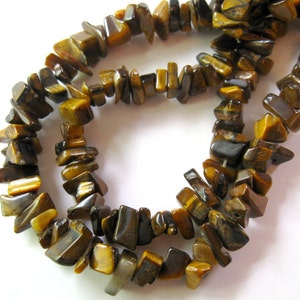 K&ouml;nnte beinhalten: Eine Str&auml;hne aus braunen und goldenen Tigerauge-Edelsteinkugeln. Die Kugeln sind unregelm&auml;&szlig;ig geformt und haben eine nat&uuml;rliche, raue Textur.