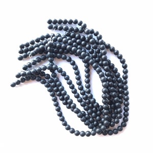 May include: A strand of black matte round beads. The beads are strung on a thin wire and are arranged in a loose pile.