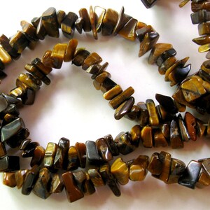 K&ouml;nnte beinhalten: Eine Schnur aus braunen und goldenen Tigerauge-Edelsteinkugeln. Die Kugeln sind unregelm&auml;&szlig;ig geformt und haben eine nat&uuml;rliche, raue Textur.
