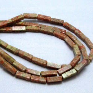 May include: A strand of green, brown, and pink rectangular gemstone beads. The beads are approximately 1/2 inch long and 1/4 inch wide.