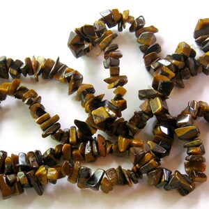 K&ouml;nnte beinhalten: Eine Str&auml;hne aus braunen und goldenen Tigerauge-Edelsteinkugeln. Die Kugeln sind unregelm&auml;&szlig;ig geformt und haben eine nat&uuml;rliche, raue Textur.