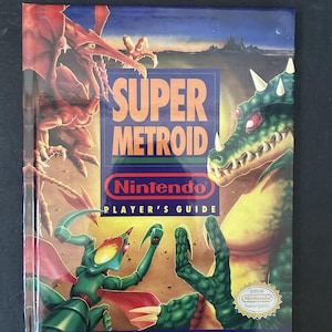 May include: A Super Metroid Player's Guide book. The cover features a vibrant illustration of a red dragon-like creature and a green monster. The title "SUPER METROID" is prominently displayed, with the Nintendo logo and "PLAYER'S GUIDE" text.