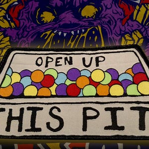 May include: White embroidered patch with a black border. The patch features a cartoon image of a box filled with colorful balls. The text "OPEN UP THIS PIT" is written in black on the box.