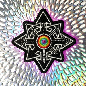 May include: Black embroidered patch with a white outline, featuring a star-like design with arrows and a rainbow-colored center. The patch is set against a shimmering, iridescent background, creating a striking contrast. This patch is suitable for jackets, bags, or other fabric items.