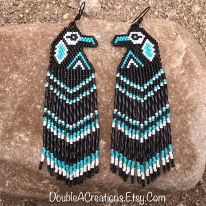 May include: A pair of long, beaded earrings with a black, white, and turquoise design. The earrings feature a stylized bird design at the top and dangle down to about 4 inches in length.