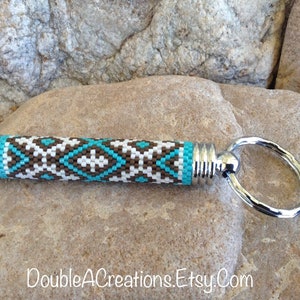 May include: A beaded keychain with a brown, white, and turquoise geometric pattern. The keychain has a silver metal ring and a silver metal cap on each end.