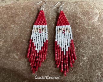 May include: A pair of red and white beaded earrings with a Santa Claus face design. The earrings are long and dangle, with a fringe of beads at the bottom.