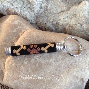 May include: A black beaded keychain with a paw print and bone design. The keychain has a silver metal ring.
