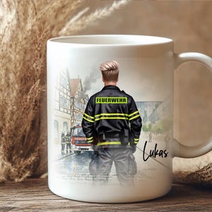 May include: White ceramic mug featuring a firefighter illustration. The design shows a firefighter in uniform with the word "FEUERWEHR" on the back. The mug also has the name "Lukas" written on it.