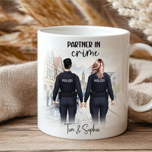 Könnte beinhalten: Ein weißer Keramikbecher mit einer aufgedruckten Illustration von zwei Polizeibeamten in dunkler Uniform mit der Aufschrift POLIZEI auf dem Rücken, die in einer Straße stehen. Der Text PARTNER IN crime und die Namen Tim & Sophia sind aufgedruckt.
