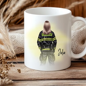 May include: White ceramic mug featuring a firefighter illustration. The design shows a person in a black uniform with yellow stripes and the word "FEUERWEHR". The name "Julia" is written in cursive. The mug is on a wooden surface.