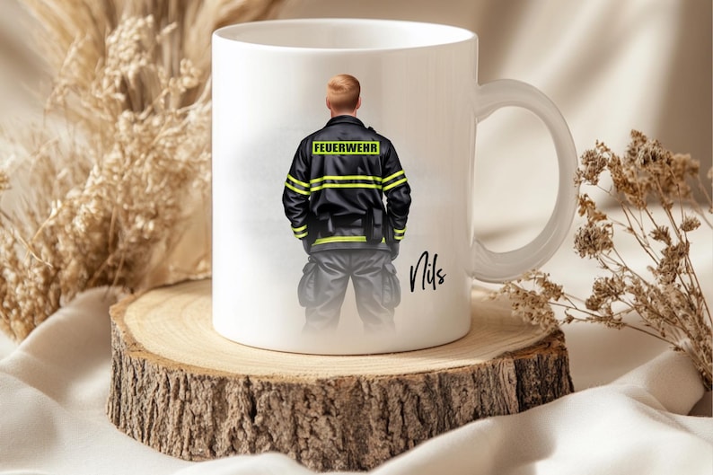 May include: White ceramic mug featuring a firefighter illustration. The firefighter is wearing a black jacket with yellow stripes and the word "FEUERWEHR". The mug is on a wooden slice, with the name "Nils" written on the mug.