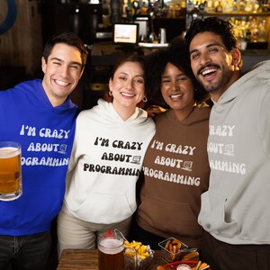 May include: Four friends wearing hoodies with the text "I'm crazy about programming" in a retro font. The hoodies are in blue, white, brown, and gray. The friends are smiling and holding drinks.