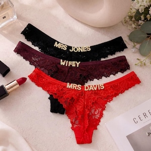 May include: Three pairs of lace thong underwear in black, burgundy, and red. Each pair features gold-toned rhinestone lettering on the front waistband. The black pair reads MRS JONES, the burgundy pair reads WIFEY, and the red pair reads MRS DAVIS.
