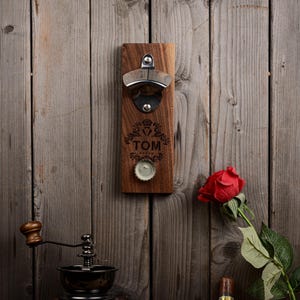 Puede incluir: Un abridor de botellas de madera para montar en la pared con un abridor de botellas plateado y una inscripción personalizada que dice "TOM".