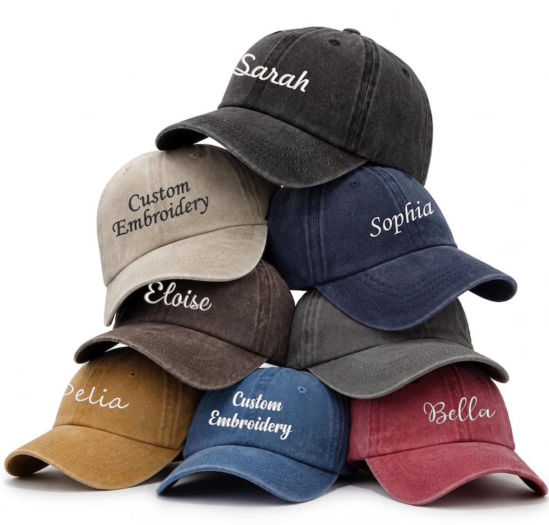 May include: A stack of baseball caps in various colors, including black, tan, navy, and red. Each cap features custom embroidery with names or the phrase "Custom Embroidery" in white script. The caps have a classic, worn look.
