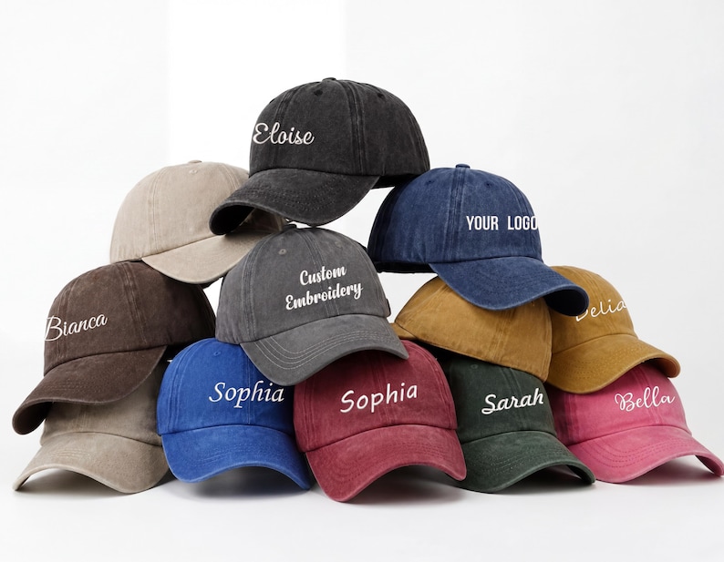 May include: A collection of ten baseball caps in various colors, including black, brown, blue, and pink. Each cap features custom embroidery with names or text like "Eloise," "Sophia," and "Your Logo." The caps are arranged in a visually appealing display.