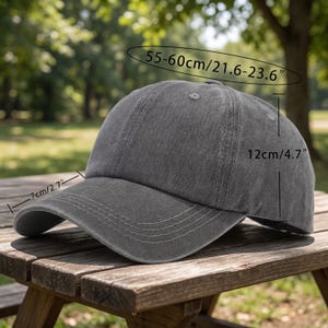 May include: A gray baseball cap with a curved brim, measuring 7 inches (17.8 cm) long. The cap is 4.7 inches (12 cm) high and has a circumference of 21.6-23.6 inches (55-60 cm). The hat is made of a soft material and is sitting on a wooden surface.