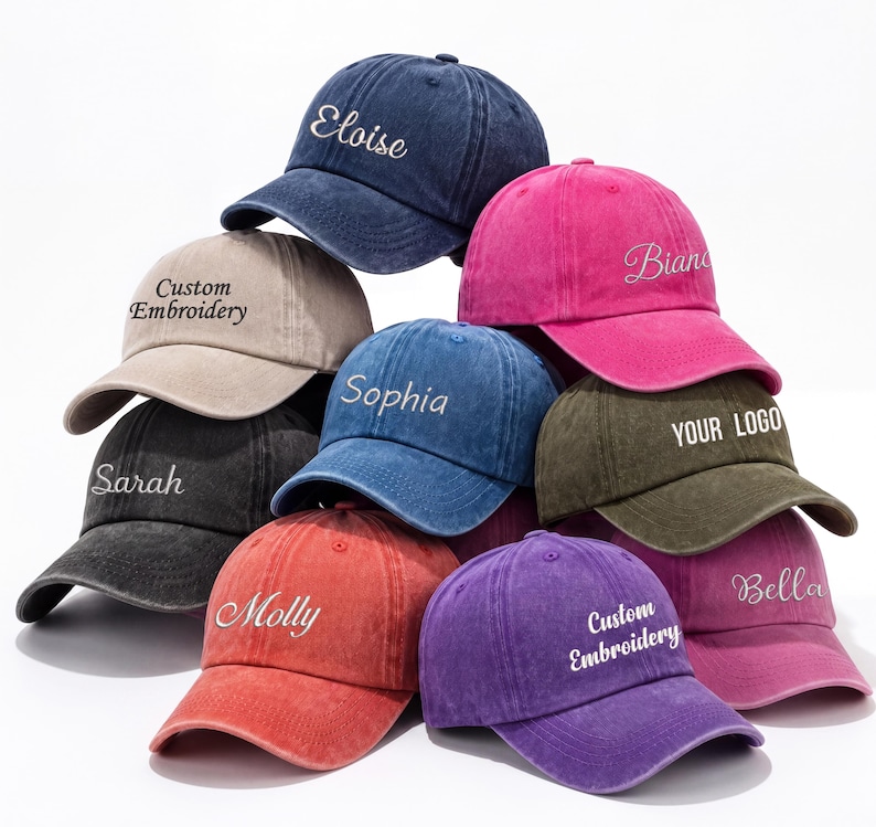May include: A collection of baseball caps in various colors, including navy, pink, red, and purple. Each cap features embroidered text, such as names and the phrase "Custom Embroidery". The caps are stacked, showcasing their design.