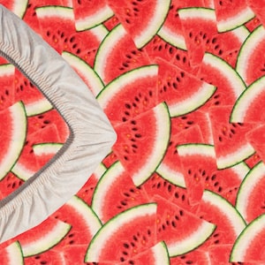 May include: A white fabric ring with a ruffled edge sits on top of a background of red watermelon slices. The watermelon slices are arranged in a random pattern.