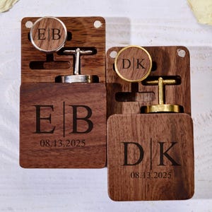 May include: Two wooden cufflink boxes with personalized initials and a date. One box has silver cufflinks with the initials "EB" and the date "08.13.2025". The other box has gold cufflinks with the initials "DK" and the same date.