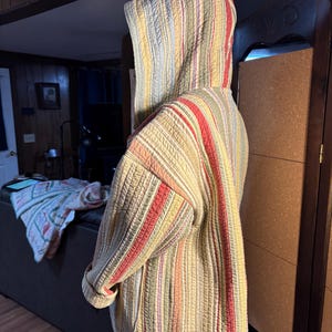 May include: Quilted jacket with a hood, featuring vertical stripes in red, yellow, green, and beige. The jacket has a relaxed fit and a quilted texture, suitable for casual wear. The design includes a hood and a full-length zipper.