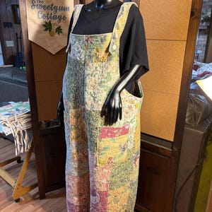 May include: A patchwork jumpsuit in a variety of floral patterns, featuring a mix of pink, green, and yellow hues. The jumpsuit has large pockets and button details. The mannequin is wearing a black t-shirt underneath.