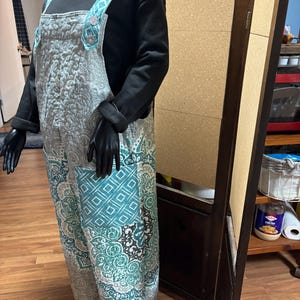 May include: A mannequin displays a pair of patterned overalls with a black long-sleeve shirt. The overalls feature a quilted design in shades of gray, teal, and white. The straps and pockets have a teal geometric pattern. The overall length is approximately 58 inches.