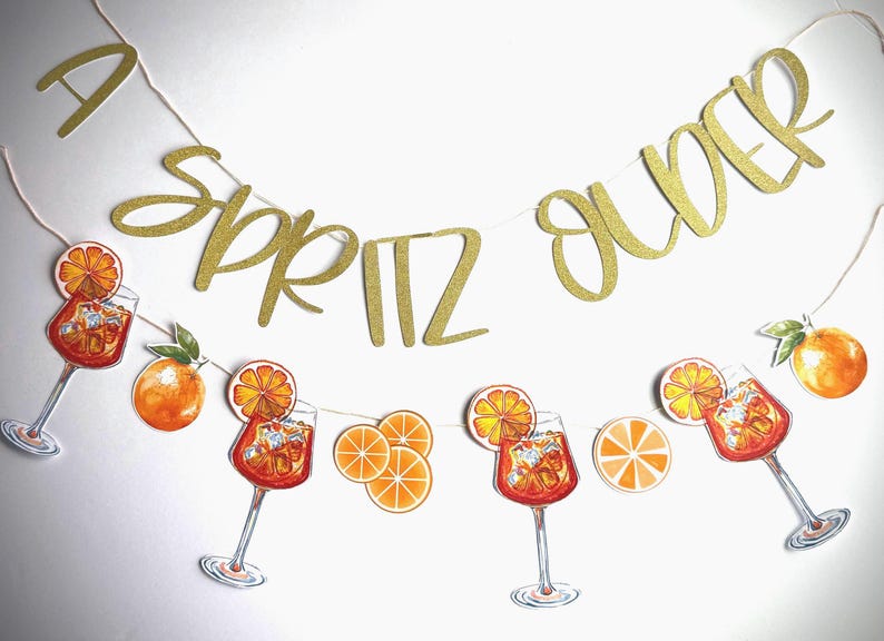 May include: A gold glitter banner that reads "A Spritz Over" strung above illustrations of Aperol spritz cocktails and orange slices. The banner and illustrations are on a white background.