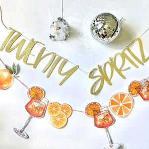 May include: A festive banner with the words "TWENTY SPRITZ" in gold glitter script. The banner is adorned with orange slice and cocktail illustrations. A disco ball and decorative light hang above.