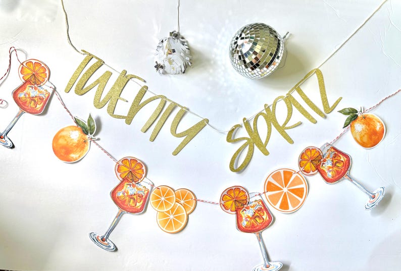 May include: A festive banner with the words "TWENTY SPRITZ" in gold glitter script. The banner is adorned with orange slice and cocktail illustrations. A disco ball and decorative light hang above.