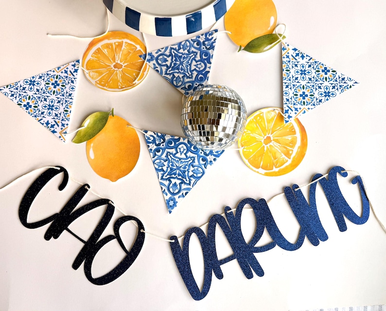 May include: A decorative banner featuring blue and white tile-patterned triangles, yellow lemon illustrations, and a central silver disco ball. The banner includes dark blue glittery script text that reads "CIAO DARLING" strung together on a white cord.