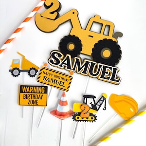 May include: A collection of construction-themed birthday cake toppers. Includes a yellow excavator, dump truck, and construction signs that read "Happy Birthday Samuel" and "Warning Birthday Zone." Also features a traffic cone and a hard hat.