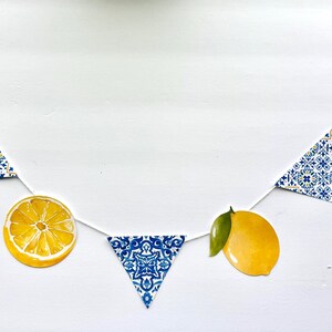 May include: A decorative garland featuring alternating shapes strung on a white cord. The elements include yellow lemon illustrations with green leaves, yellow lemon slices, and triangular pennants with a blue and white geometric tile pattern.