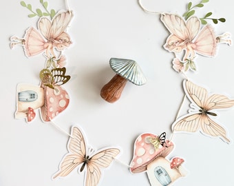 May include: A whimsical garland featuring fairy and butterfly cutouts, mushroom accents, and small fairy houses. The garland is strung on a white cord. The color palette includes soft pinks, browns, and greens, creating a delicate and enchanting aesthetic.