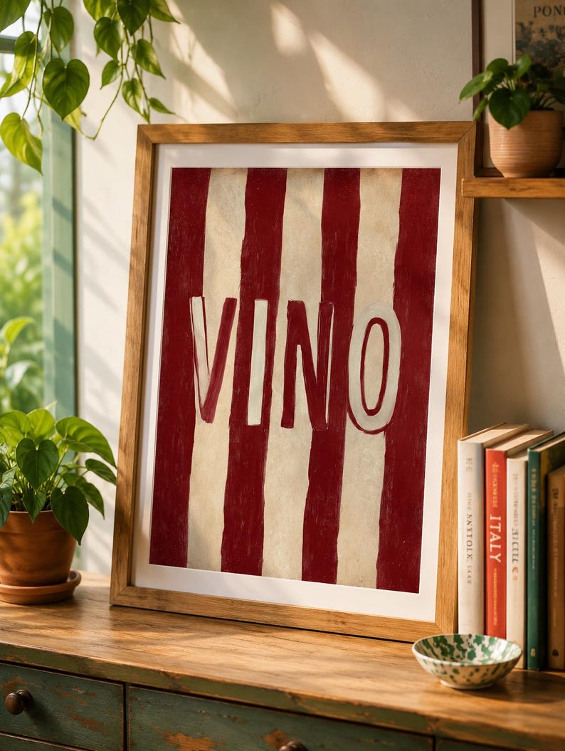 Op de afbeelding: Een ingelijst kunstwerk met een rood-witte gestreepte achtergrond en het woord "VINO" in wit. De houten lijst complementeert het kunstwerk, dat op een houten oppervlak wordt getoond. Een decoratief stuk voor een huis.