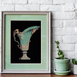 May include: Framed print of an antique teal and gold decorative urn against a black background. The urn has ornate details and a curved spout. The frame is a light green color. The print is displayed on a wooden surface with a white brick wall backdrop.