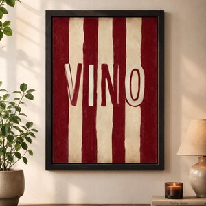Op de afbeelding: Zwart omlijst kunstwerk met rode en cr&egrave;mekleurige verticale strepen en het woord "VINO" in witte letters. Het kunstwerk hangt aan de muur boven een houten oppervlak.