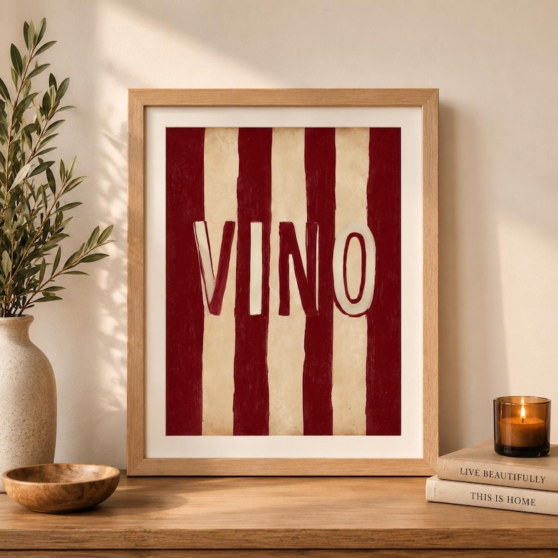 Op de afbeelding: Houten ingelijst kunstwerk met een rood en cr&egrave;me gestreept ontwerp. Het woord "VINO" wordt weergegeven in een vetgedrukte, witte, omlijnde letter. Het kunstwerk wordt getoond op een houten oppervlak.