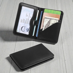 Può includere: Portafoglio bi-fold in pelle nera, aperto per mostrare una patente di guida, carte di credito e una banconota da cento dollari USA. Il portafoglio è mostrato aperto e chiuso, rivelando i suoi scomparti interni e il design esterno.