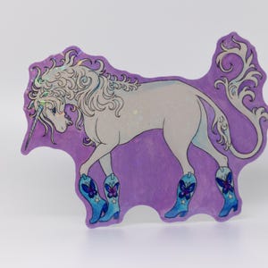 May include: A whimsical illustration of a unicorn wearing blue cowboy boots with butterfly designs. The unicorn is white with a silver horn and mane, set against a purple background with decorative swirls.