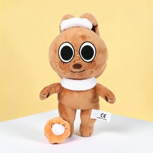 May include: A brown plush bunny with large black eyes, a white collar, and a matching headband. A small orange plush donut with a white center sits in front of the bunny. A white tag with black text is attached to the bunny.