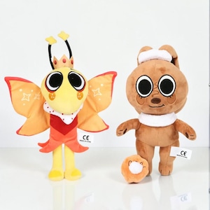 May include: Two plush toys: a yellow and orange butterfly creature with a crown and a brown bunny with a white scarf. Both have large, round eyes and are standing on a white surface. Each has a small tag.