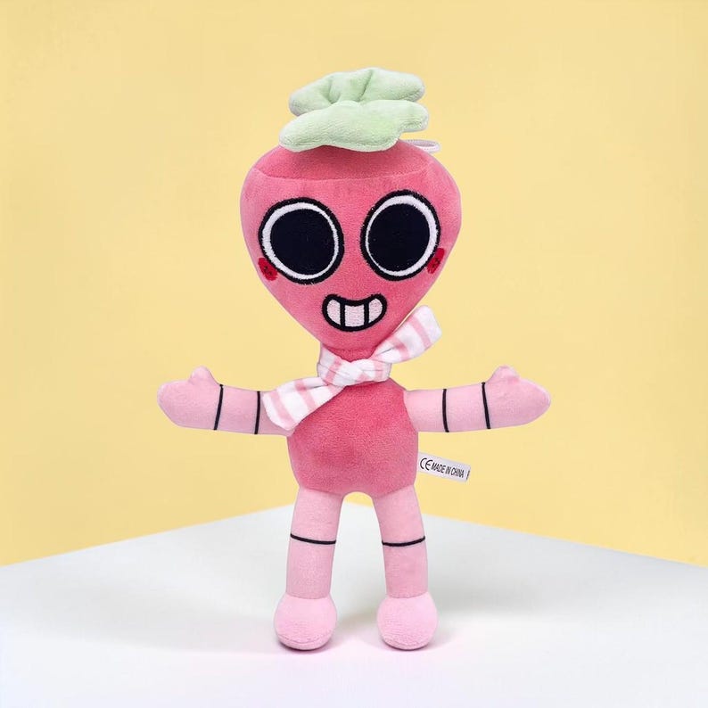 May include: A pink plush toy in the shape of a radish with a smiling face, large black eyes, and a striped scarf. The toy has outstretched arms and a green leafy top. The toy is standing on a white surface against a yellow background.