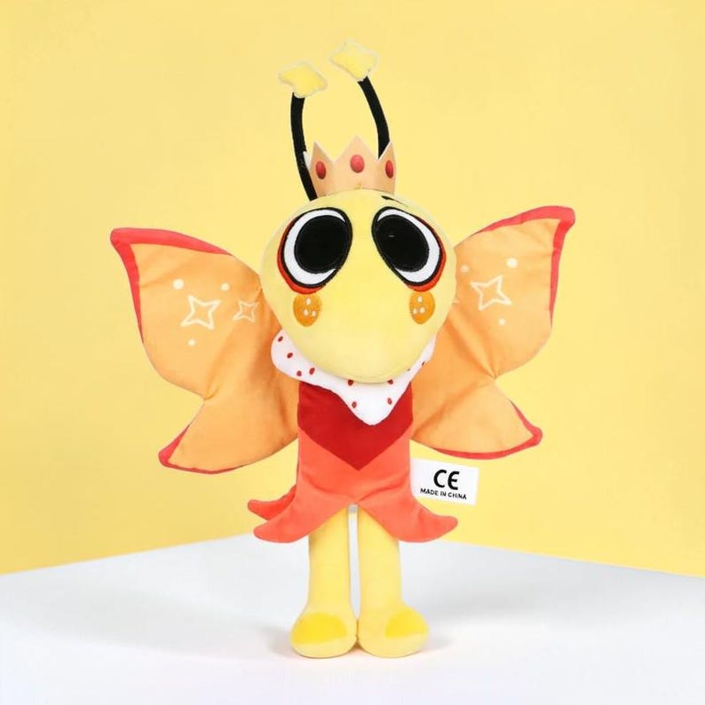 May include: A plush toy in the shape of a yellow insect with large black eyes, orange wings, and a red and white collar. The toy has a crown and two antennae. The wings have white star details. The toy is on a yellow background.