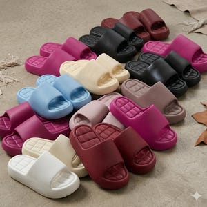 Op de afbeelding: Een verzameling kleurrijke instappers in diverse tinten, waaronder wit, crème, blauw, roze, bordeauxrood en zwart. De sandalen hebben een eenvoudig, modern ontwerp met een enkele band en een getextureerd voetbed. De afbeelding toont een verscheidenheid aan maten en kleuren.