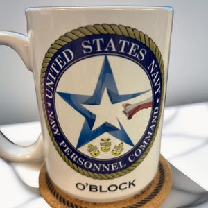 May include: White ceramic mug with a navy blue and gold seal that reads "United States Navy Navy Personnel Command" and a blue star with a red, white, and blue airplane. The mug also has the text "O'Block" printed on the bottom.