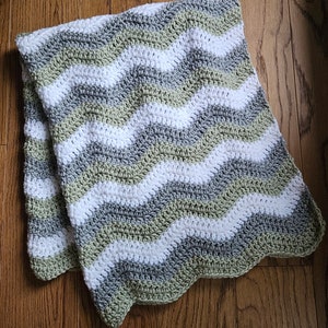 May include: A crocheted baby blanket with a wavy pattern in shades of green, gray, and white.